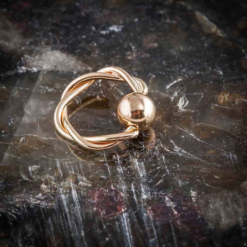 14K rose gold twisted fixed bead ring resting on dark stone surface, angled view showing bead detail