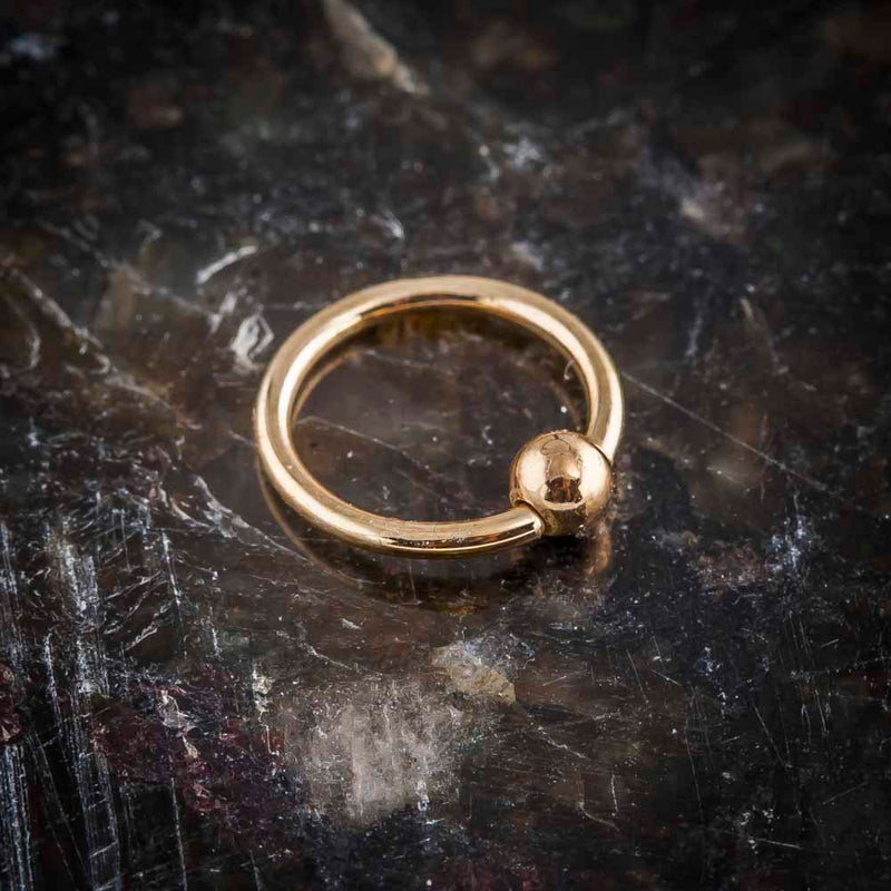 14K rose gold fixed bead ring on dark stone surface, angled view showing warm gold tone