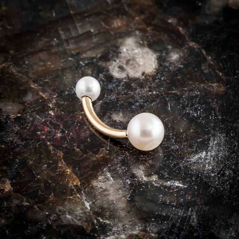 14k yellow gold dual cultured pearl navel ring displayed on dark stone surface, angled view