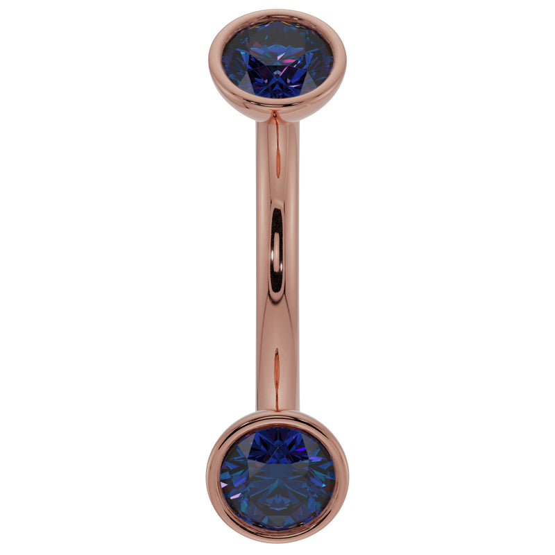 Close-up of 14k rose gold curved barbell highlighting deep blue sapphire bezel ends