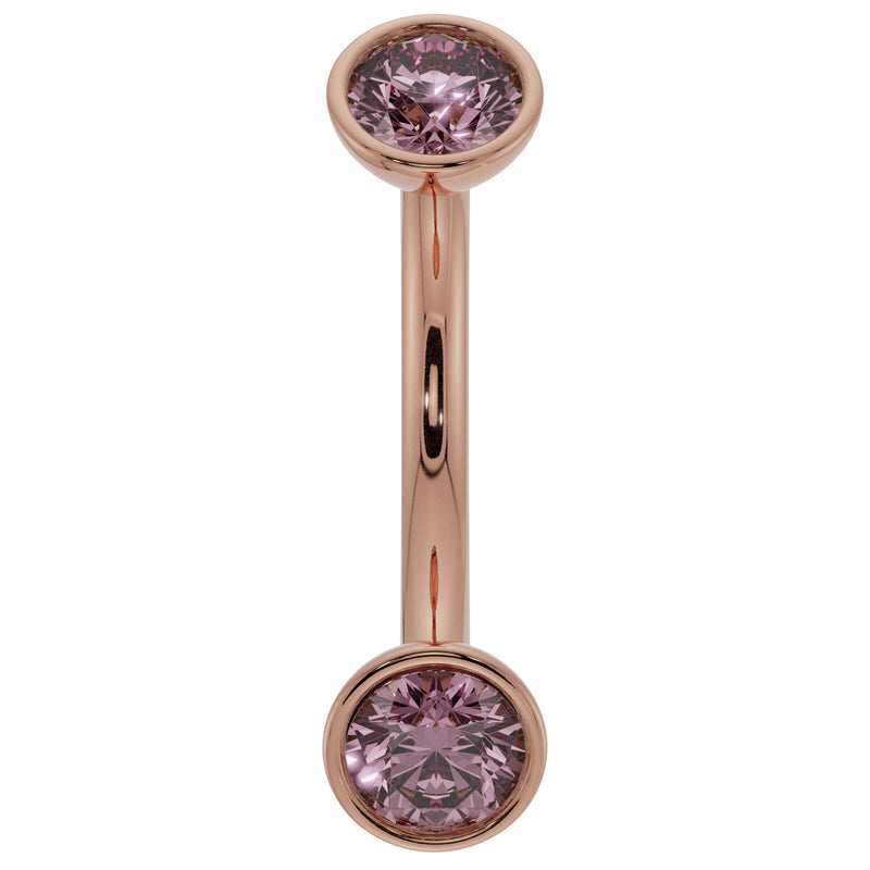 Close-up of 14K rose gold curved barbell with larger bezel-set pink sapphire ends, front view