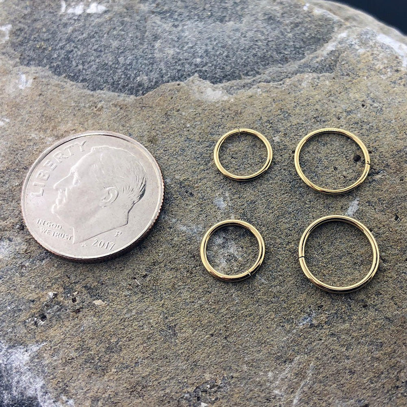 Four 14k yellow gold seam ring hoops in small sizes shown next to a dime for scale reference
