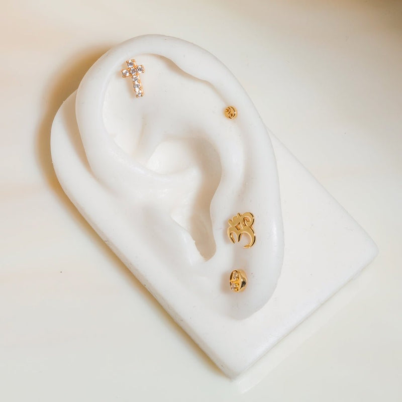 Diamond cross gold labret stud on white ear display in helix placement among mixed gold piercing jewelry