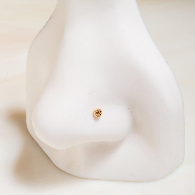 Tiny 4mm 14k yellow gold yin yang stud shown on white nose mannequin for nostril piercing scale