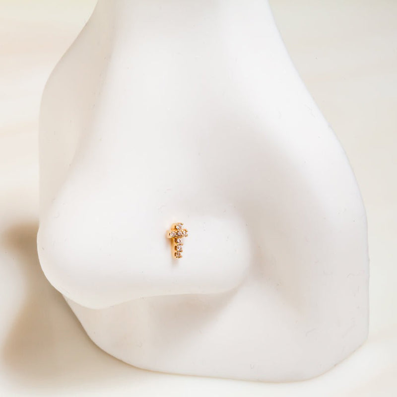 Tiny 14k gold diamond cross flat back stud shown on a ceramic nose model for size and placement reference