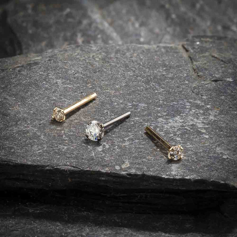 Three CZ straight post nose studs in mixed gold tones arranged on dark slate surface