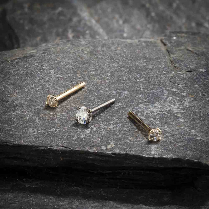 Three 3mm CZ straight post nose rings in yellow and white gold shown on textured stone surface