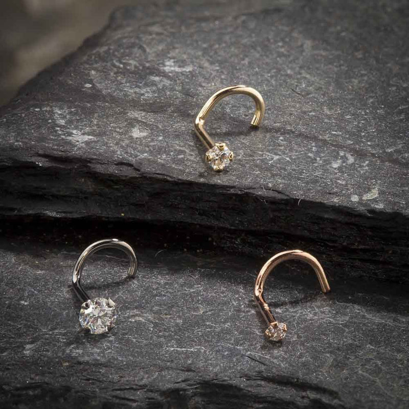All three metal options of 14k gold CZ twist nose rings — yellow, white, and rose gold on dark stone