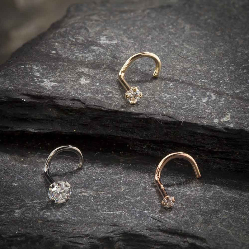Three CZ twist nose rings in yellow, white, and rose gold displayed on dark slate surface