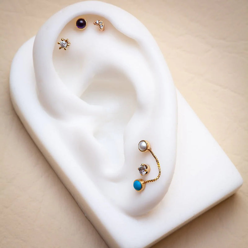 14k gold CZ prong-set flat back stud styled on white ear display with mixed piercing jewelry curation