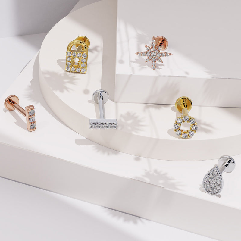 14K gold diamond halo labret styled in a flat lay with other diamond flat back earring designs