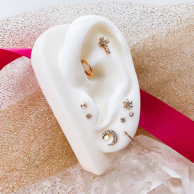 Diamond flower stud among gold celestial ear piercing stack on white mannequin with glitter background