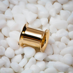 Single 14k yellow gold double flare ear tunnel resting on white pebbles, lifestyle close-up