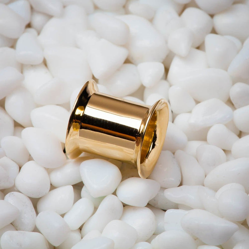 Single 14k yellow gold double flare ear tunnel resting on white pebbles, lifestyle close-up
