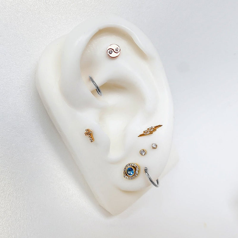 Evil eye blue topaz flat back stud in lobe piercing on white ear mannequin with mixed metal curated stack