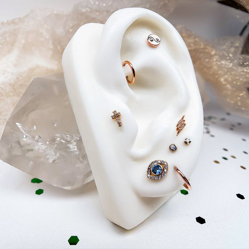 14k rose gold diamond cross stud styled in helix position on white ear form in a curated multi-piercing display