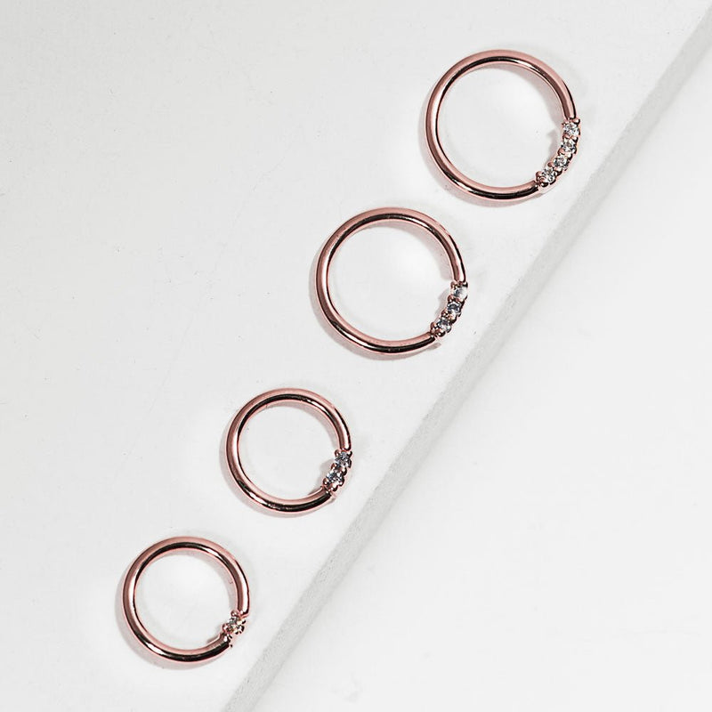Four 14K rose gold diamond seam rings in graduated sizes arranged diagonally on white surface