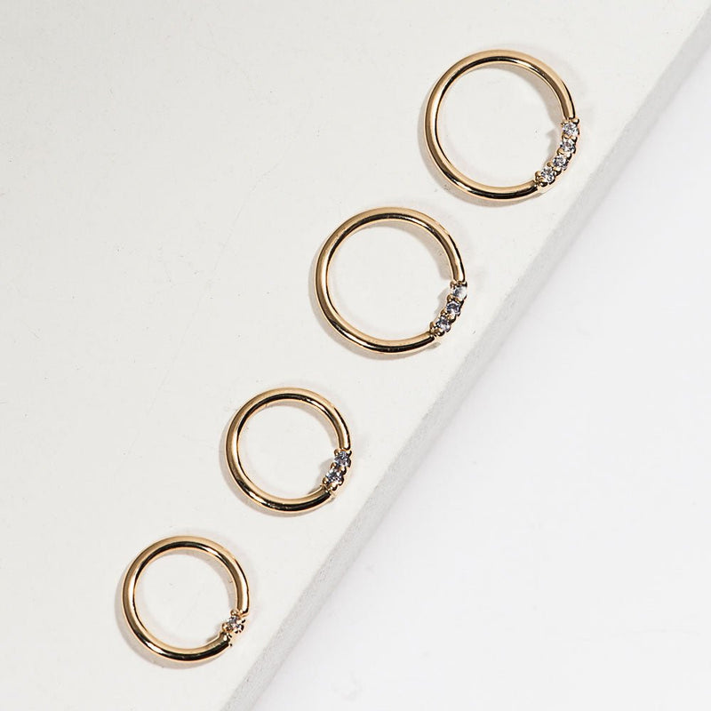 Four 14K yellow gold diamond seamless hoops in graduating sizes arranged on white surface