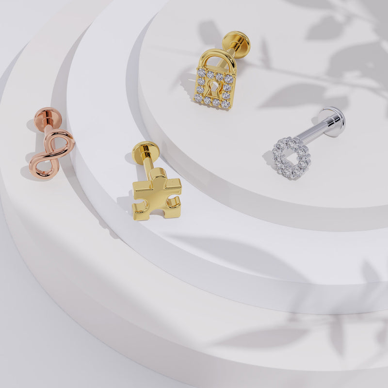 14K yellow gold puzzle piece flat back labret displayed on tiered white surface with other gold charm earrings