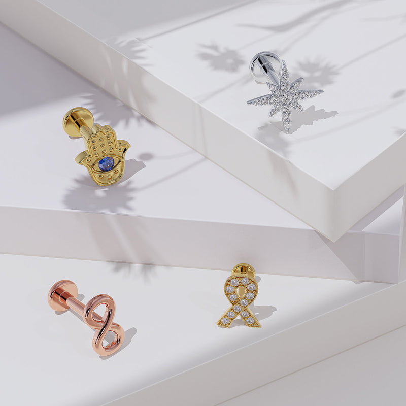 14K rose gold infinity flat back earring displayed among assorted gold labret studs on white surface