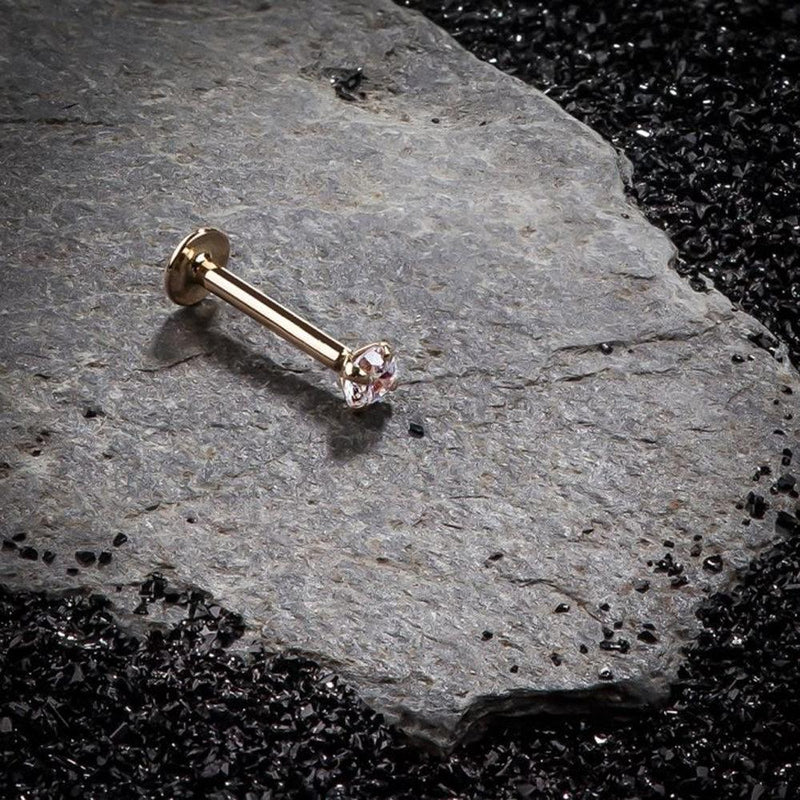 14k rose gold CZ flat back labret stud resting on dark stone surface, editorial lifestyle shot