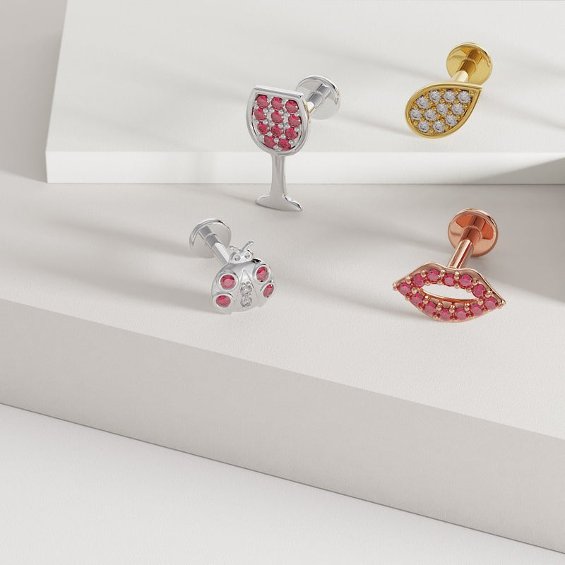 14K rose gold lips labret alongside silver ladybug and wine glass flat back earrings on display