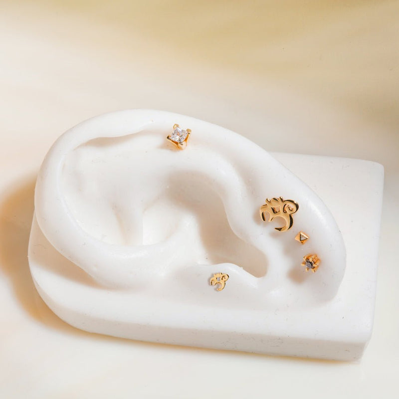 14k gold Om flat back stud on white ceramic ear model styled with assorted gold cartilage studs
