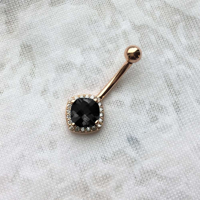 14k rose gold cushion-cut black onyx belly ring with diamond halo, angled view on textured surface