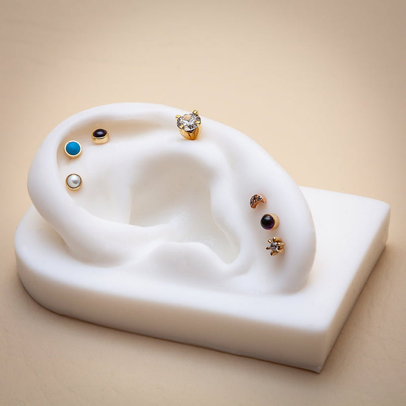 Pearl cabochon flat back stud on white ear mold alongside turquoise, onyx, and CZ gold studs