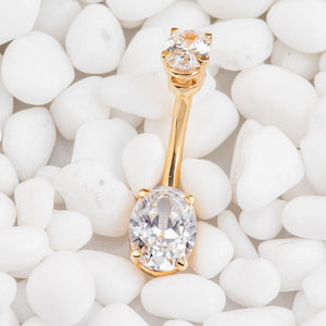 14k yellow gold oval CZ navel ring resting on white pebbles, lifestyle shot