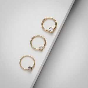 Three 14k yellow gold princess-cut CZ fixed bead rings in graduating hoop sizes on grey surface