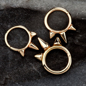 Three 14K rose gold triple spike seam rings in varying sizes shown on dark stone surface