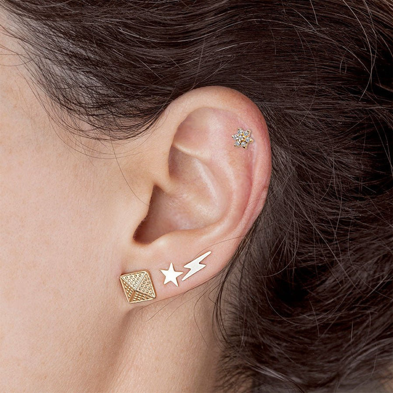 14K gold star stud earring worn in lobe piercing styled with lightning bolt and pyramid studs