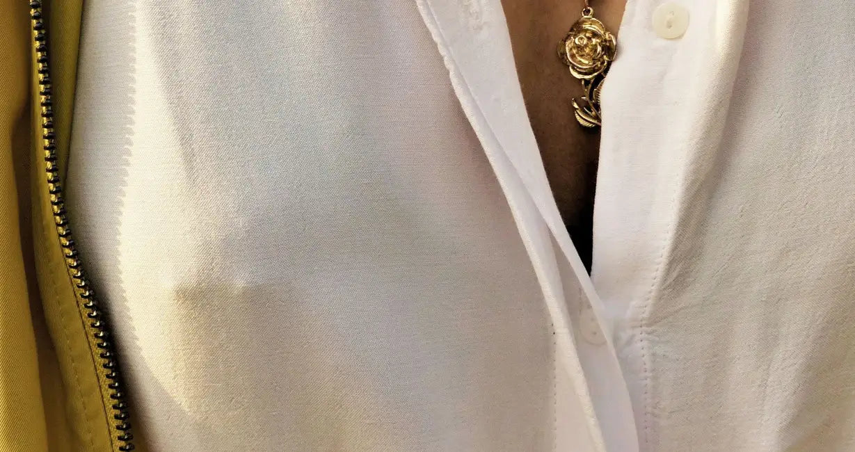 Close-up of a white shirt with a gold necklace and beige jacket.