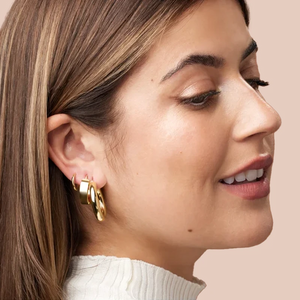 14k yellow gold huggie hoop earrings worn on model's ear, styled in a stacked multi-piercing look
