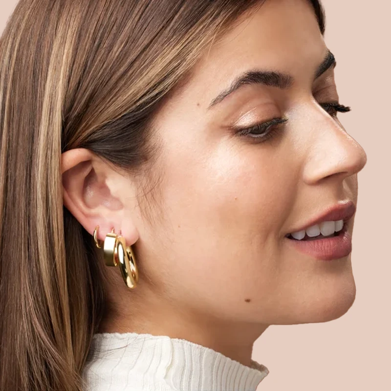 14k yellow gold huggie hoop earrings worn on model's ear, styled in a stacked multi-piercing look