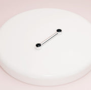 14K white gold black diamond bezel nipple barbell resting on white surface, angled lifestyle shot