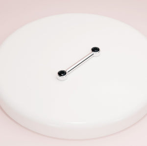 14K white gold black diamond bezel nipple barbell resting on white surface, angled lifestyle shot