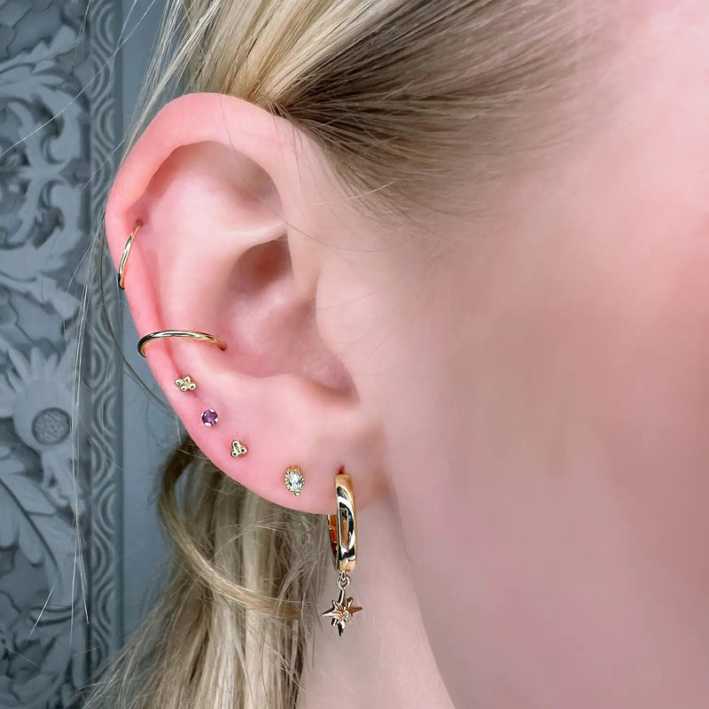 Amethyst prong-set labret worn in a helix cartilage piercing, styled with mixed gold ear stack
