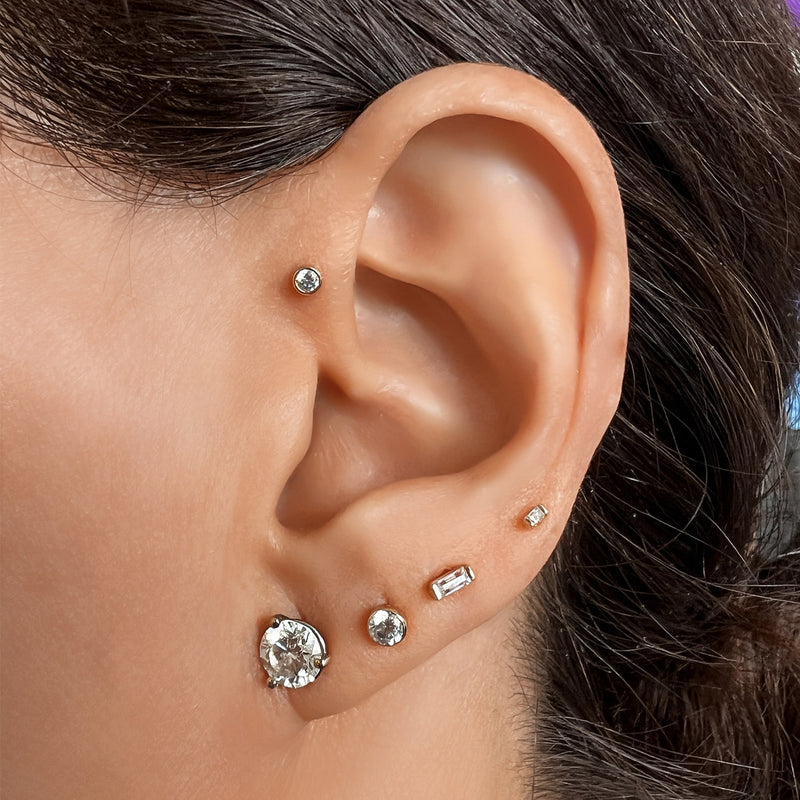 Bezel diamond stud styled in ear stack with mixed gold earrings on dark-haired model