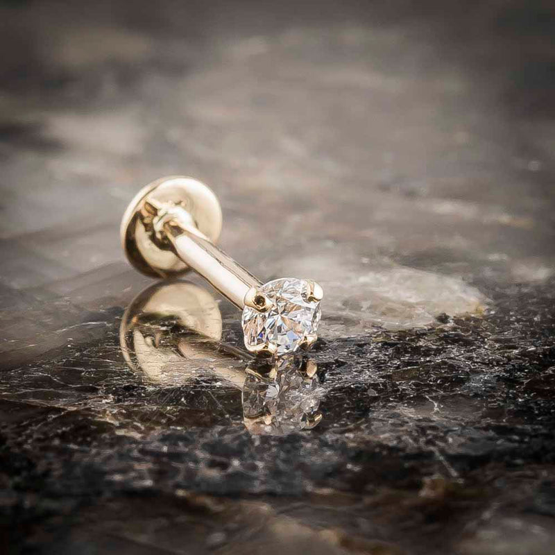 14k yellow gold 3mm diamond flat back labret stud resting on dark marble surface, angled lifestyle shot