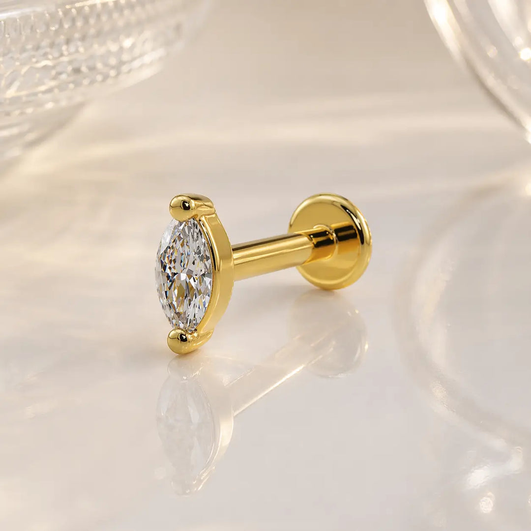 14k yellow gold 3mm marquise diamond flat back labret stud on marble surface, angled lifestyle shot