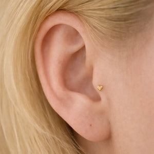 14k gold 3mm heart flat back cartilage earring worn in tragus piercing on model with blonde hair