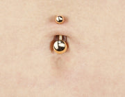 14k yellow gold double ball navel ring worn in belly piercing, close-up showing ball size contrast