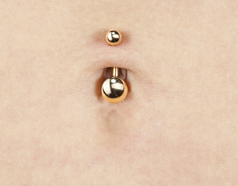 14k yellow gold double ball navel ring worn in belly piercing, close-up showing ball size contrast