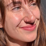 Four-diamond gold seam ring hoop in a smiling model's nostril piercing, natural light