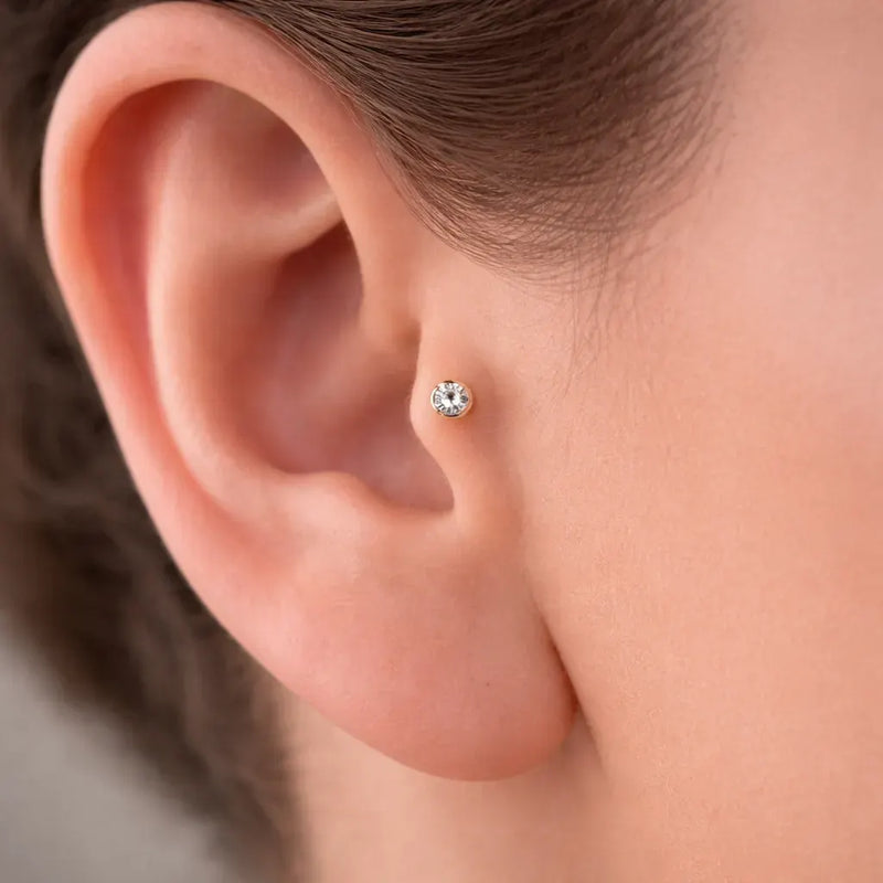 4mm CZ bezel-set 14k gold flat back labret worn in a tragus piercing, close-up fit view