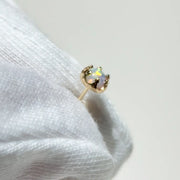 A gold crown-shaped stud earring with an iridescent opal-like center stone, held by white gloves.