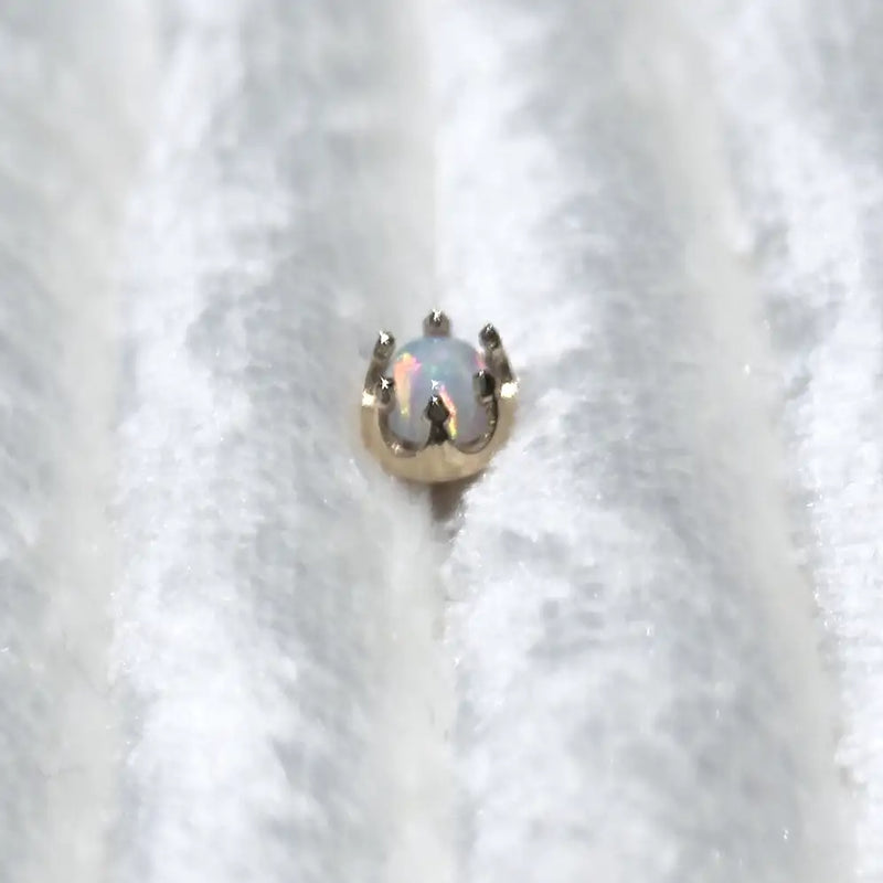 A small gold crown-shaped ring setting holding an iridescent white opal, resting on a textured white fabric background.