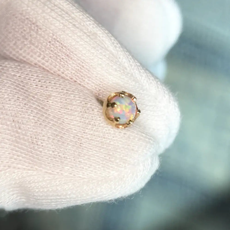 A cabochon opal gemstone with iridescent play-of-color, set in a gold bezel setting, shown resting on a white gloved finger.